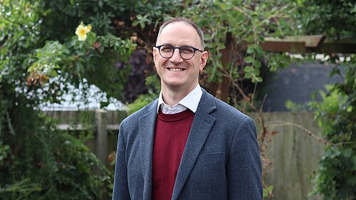 A headshot of Ian Sollom with nature in the background